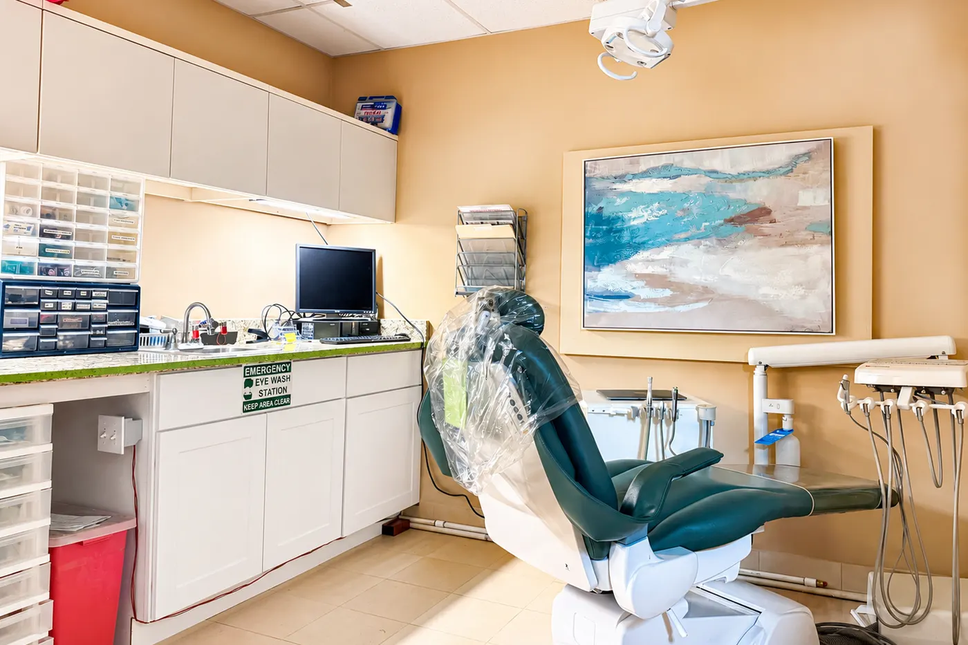 A treatment room at the clinic, with a dental chair, instrument trays, and a wall-mounted monitor.